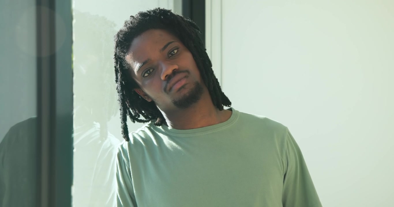 African American man by glass door in lightgreen long-sleeve shirt, tilting into sunlit reflection