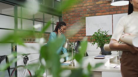 Portrait-of-happy-biracial-female-architect-holding-architectural-blueprints-at-office