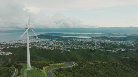 Scenic-aerial-view-of-iconic-Brooklyn-wind-turbine-overlooking-the-sprawling-landscape-of-harbour-and-hills-in-capital-city-Wellington,-New-Zealand-Aotearoa