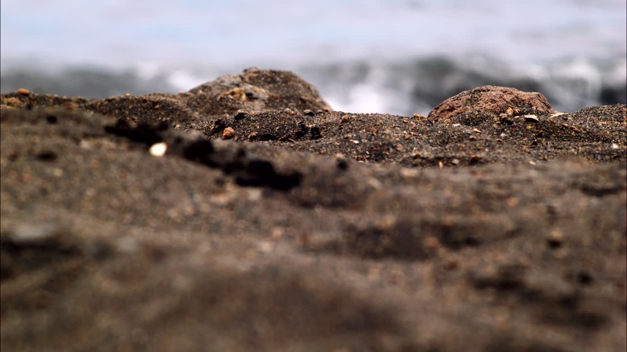Primo piano di sabbia e rocce su una spiaggia con onde dell'oceano sullo sfondo
