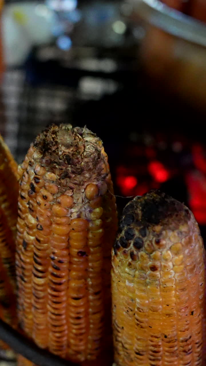 Close-up shot of corn grilling over open flames in Cali, Colombia. The warm lighting highlights the maize details, perfect for vertical video formats in social media stories