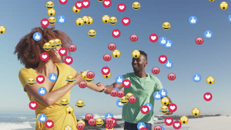 multiple digital icons floating against african american couple holding hands walking on the beach