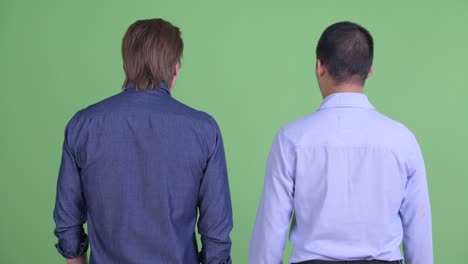 two businessman looking shocked and guilty back view shot against green studio background