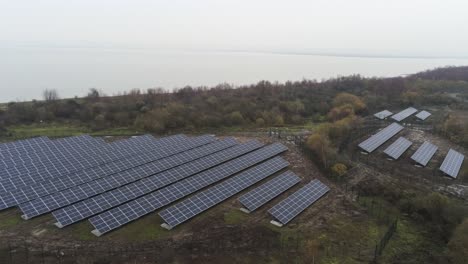Solar-panel-array-rows-aerial-view-misty-autumn-woodland-countryside-slow-pan-right