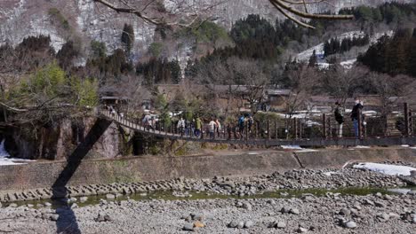 people crossing bridge over river to shirakawa-go in the mountains of gifu japan