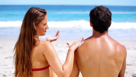 una morena aplicando protector solar a su novio.