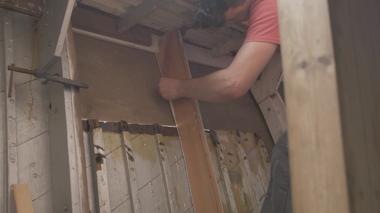 Un giovane falegname traccia il compensato per l'interno di una barca di legno.