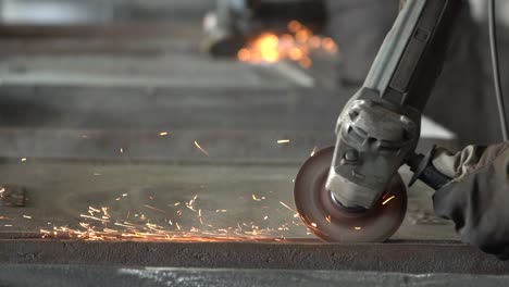 blacksmith grinding metal plates with circular saw in metal casting factory, closeup slow motion shot of sparks flying from hot metal