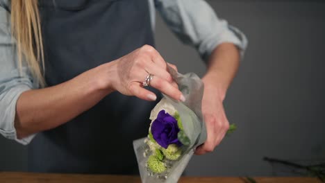 close up view of hands of female florist wrapping a bunch of flowers in decorating paper. slow motion shot