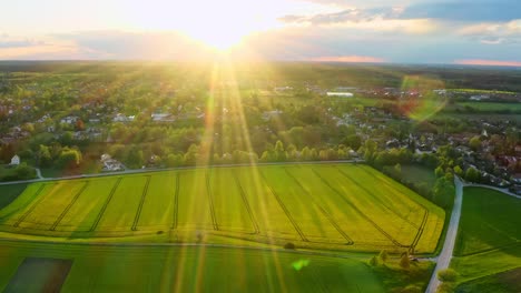 Mit-Einer-Drohne-In-Die-Sonne-Fliegen-Ein-Kleines-Dorf-Hinter-Einem-Raps-Im-Blick-Auf-Den-Frühling