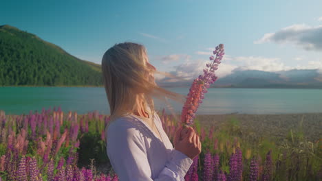 attractive blond woman picking up lupin flower and smelling petals, dreamy scene