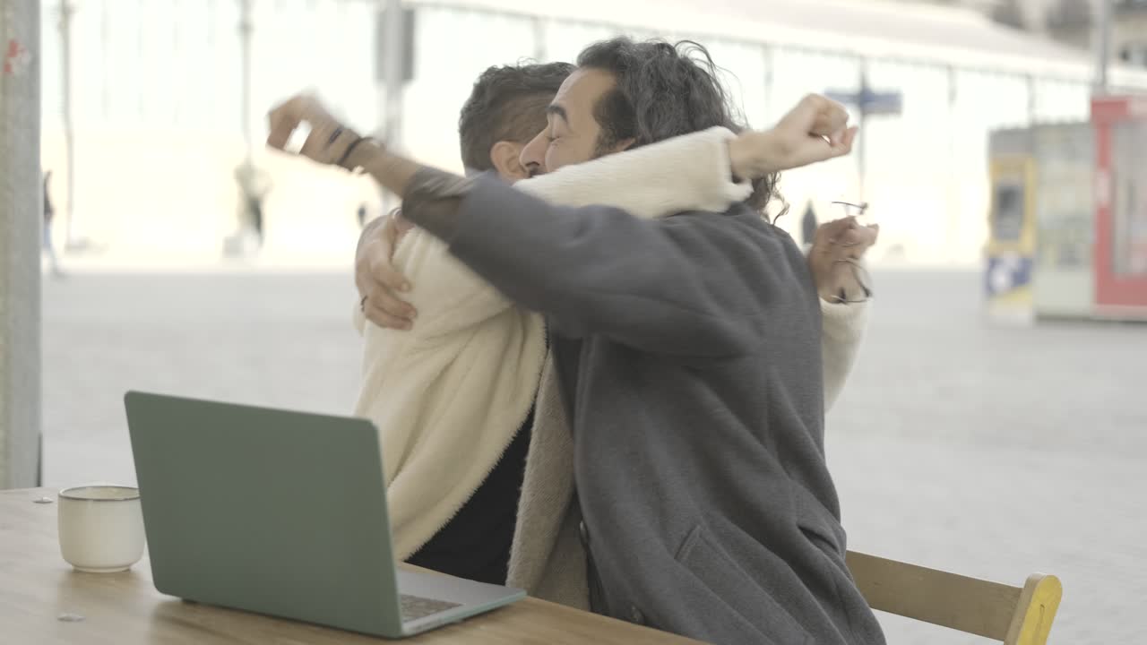 Two men celebrating success while working on a laptop outdoors