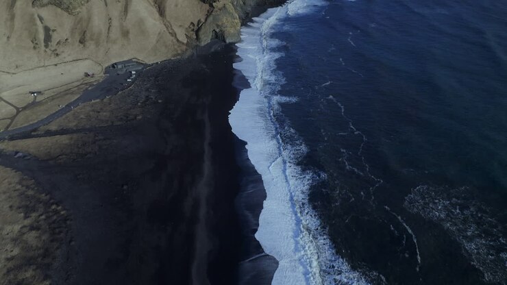 Onde bianche spumeggianti che si infrangono sulla spiaggia di sabbia nera di Reynisfjara con scogliere e faraglioni di basalto sullo sfondo nell'Islanda meridionale