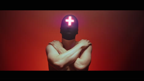 masked man with cross of light glowing on his face moves slowly