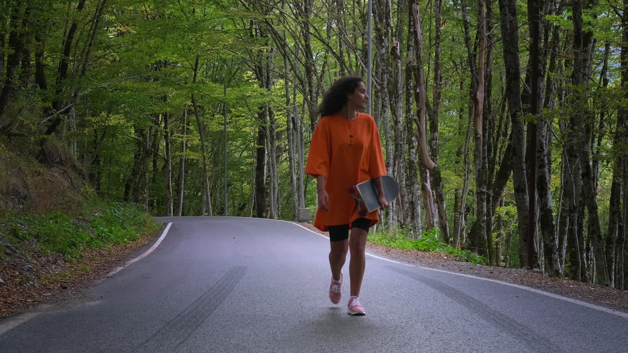 mujer caminando por un camino del bosque con una patineta