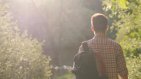 a teenager with a backpack walks through the park the sun shines into the camera beautiful glare