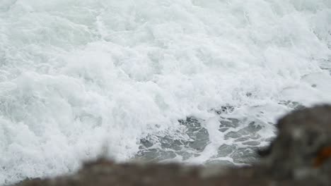 Slow-motion-wave-foam-in-tight-shot-with-rock-in-the-foreground