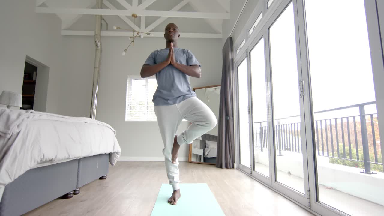 African american man doing yoga and meditating at home, slow motion