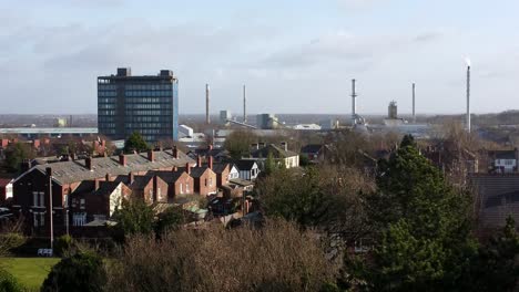 Aerial-view-over-park-trees-to-industrial-townscape-houses-with-blue-Pilkingtons-head-office,-Merseyside,-England