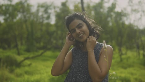 Close-up-of-happy-tan-indian-woman-fixing-hair-laughing-and-posing-in-meadow