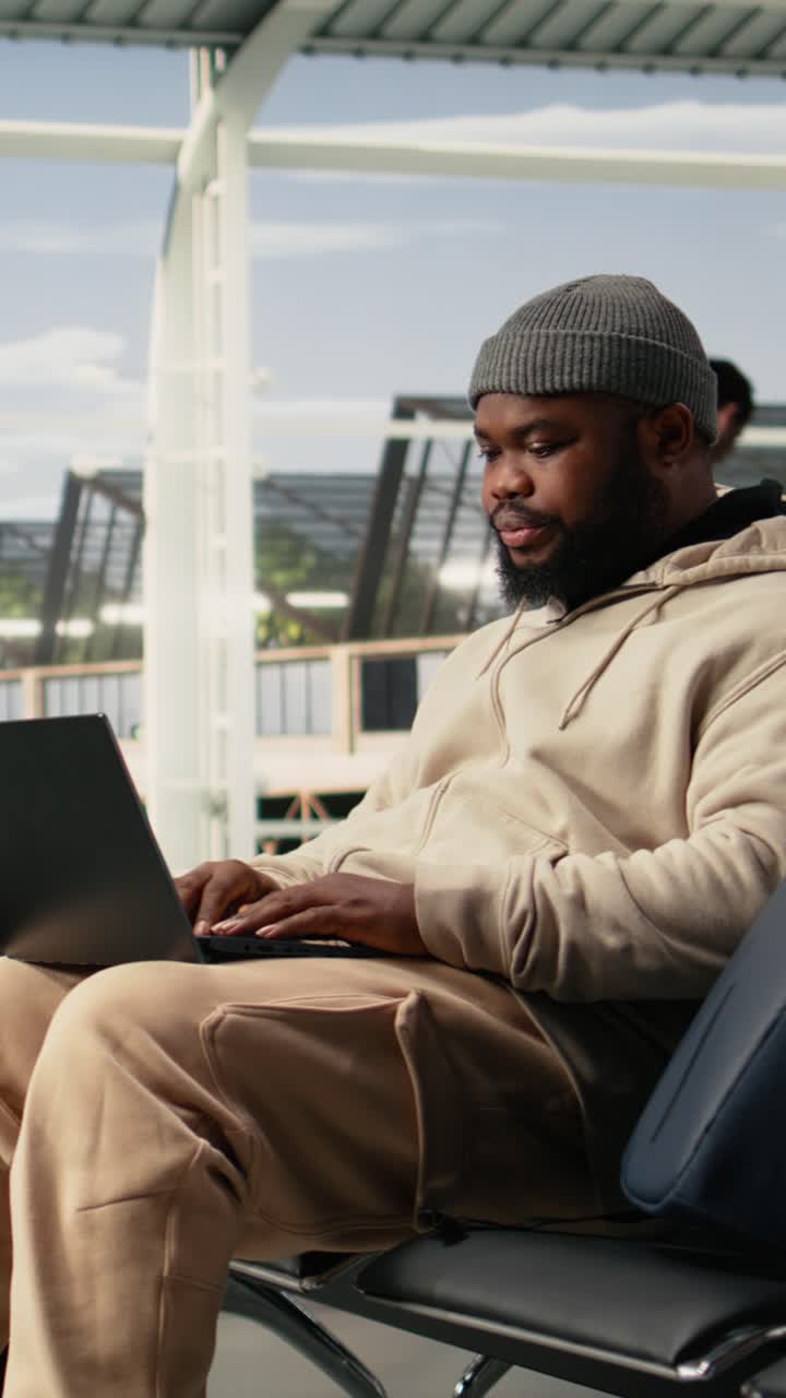 Vertical Video Black Man Digital Nomad Working On Laptop In Busy Airport Terminal Lounge