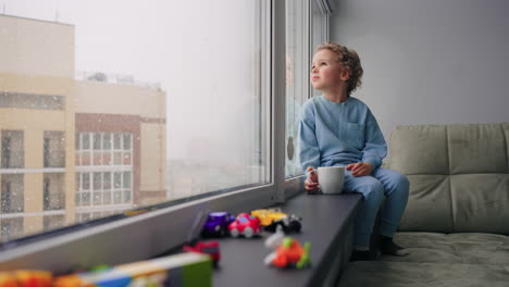 cute little boy is sitting alone in children room with many of toys cozy home atmosphere in winter weekend