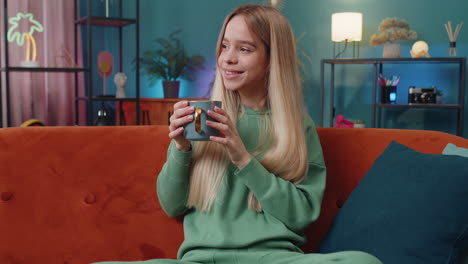 Attractive-smiling-woman-girl-drinking-a-cup-of-coffee-or-herbal-tea-at-home-couch-in-the-morning