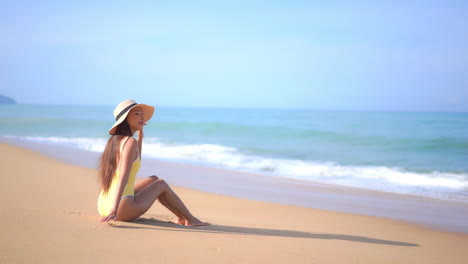 Eine-Junge-Frau-In-Einem-Gelben-Badeanzug-Sitzt-An-Einem-Sandstrand-Und-Genießt-Die-Landschaft