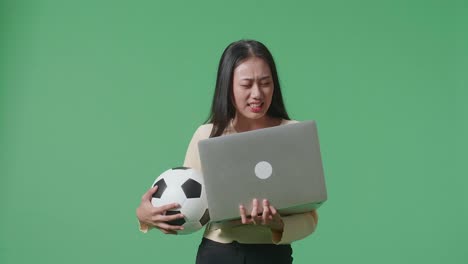 una mujer con una pelota de fútbol y una computadora portátil que parece decepcionada.