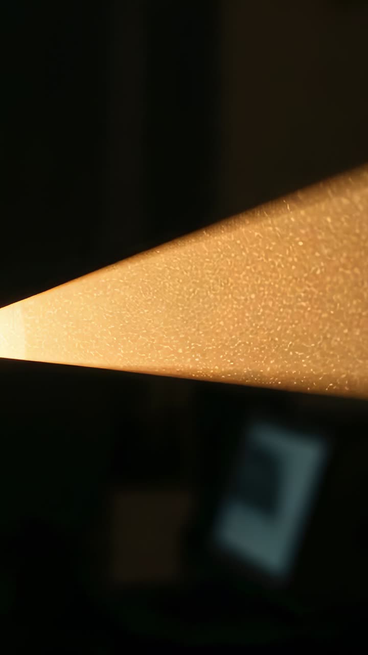 Vertical video: Projector casting beam across dim room, revealing drifting dust motes near monitor