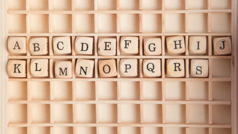 Hand-spelling-out-the-alphabet-in-wooden-dice-on-a-grid