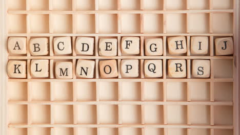 Hand spelling out the alphabet in wooden dice on a grid