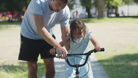 young asian father teaching daughter to ride bicycle in park