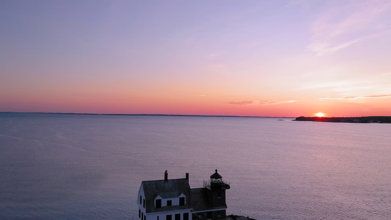 일출을 향해 눈 덮힌 바위 방파제 끝에서 등대를 지나 날아가는 항공 영상