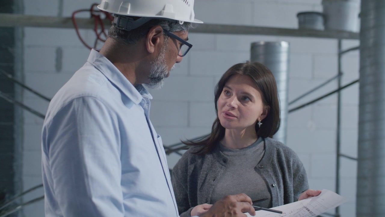 Senior Architect Presenting Building Plan to Female Client on Construction Site