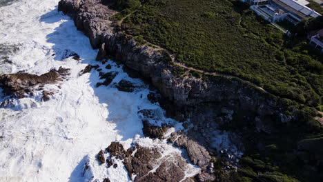 caminata por el acantilado de la costa de hermanus con agua de mar espumosa contra las rocas