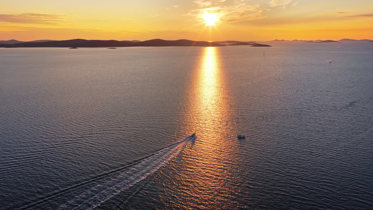 Aerial drone view of a small white speedboat cuts across deep blue water, leaving a bright trail behind it. Adriatic sea, Croatia