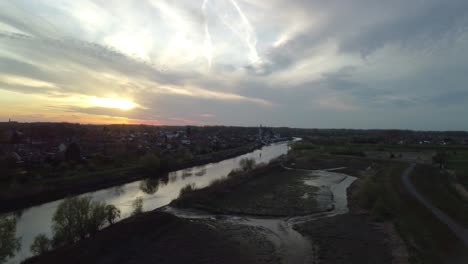 a drone pans over the river schelde and a city at sunset