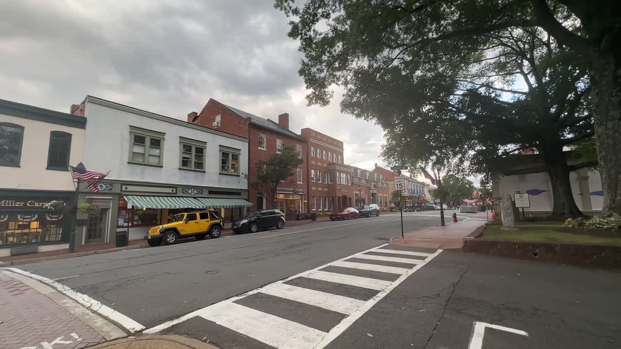 Downtown street lined with brick buildings, storefronts, and parked vehicles under cloudy sky in West Virginia historic district, capturing local charm and peaceful atmosphere
