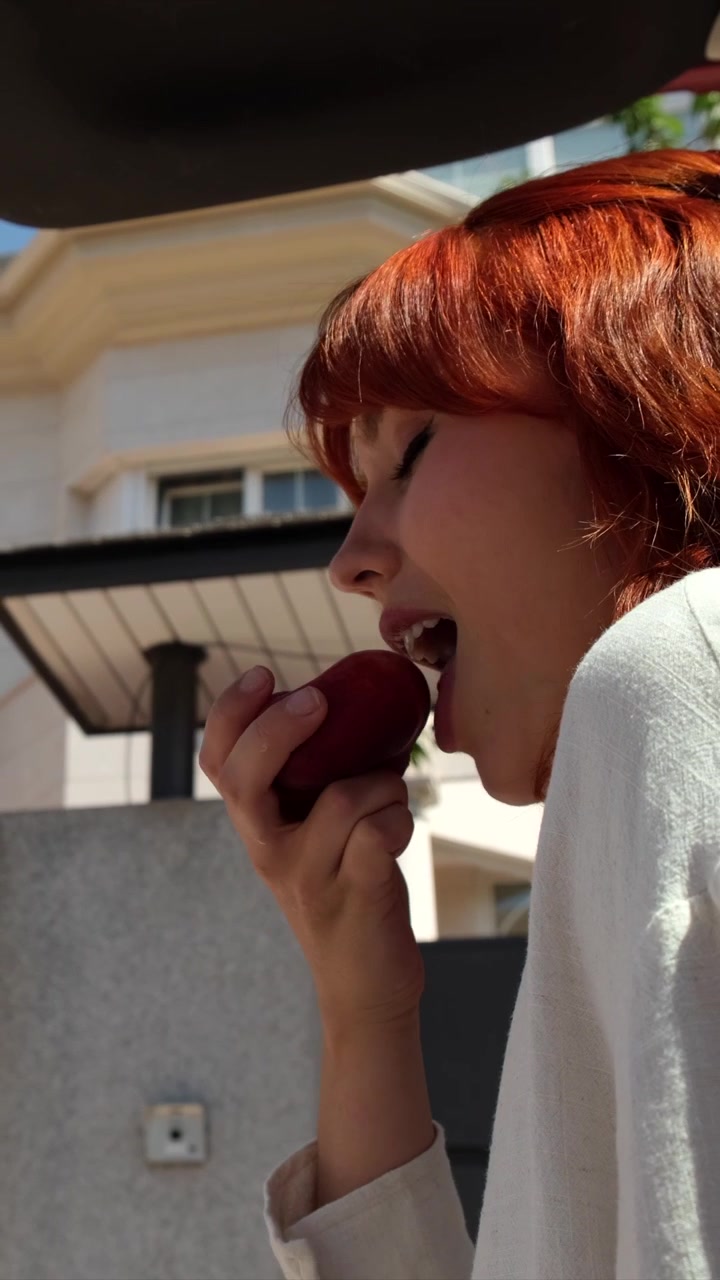 Young Woman With Red Hair Eating a Fresh Apple Outdoors