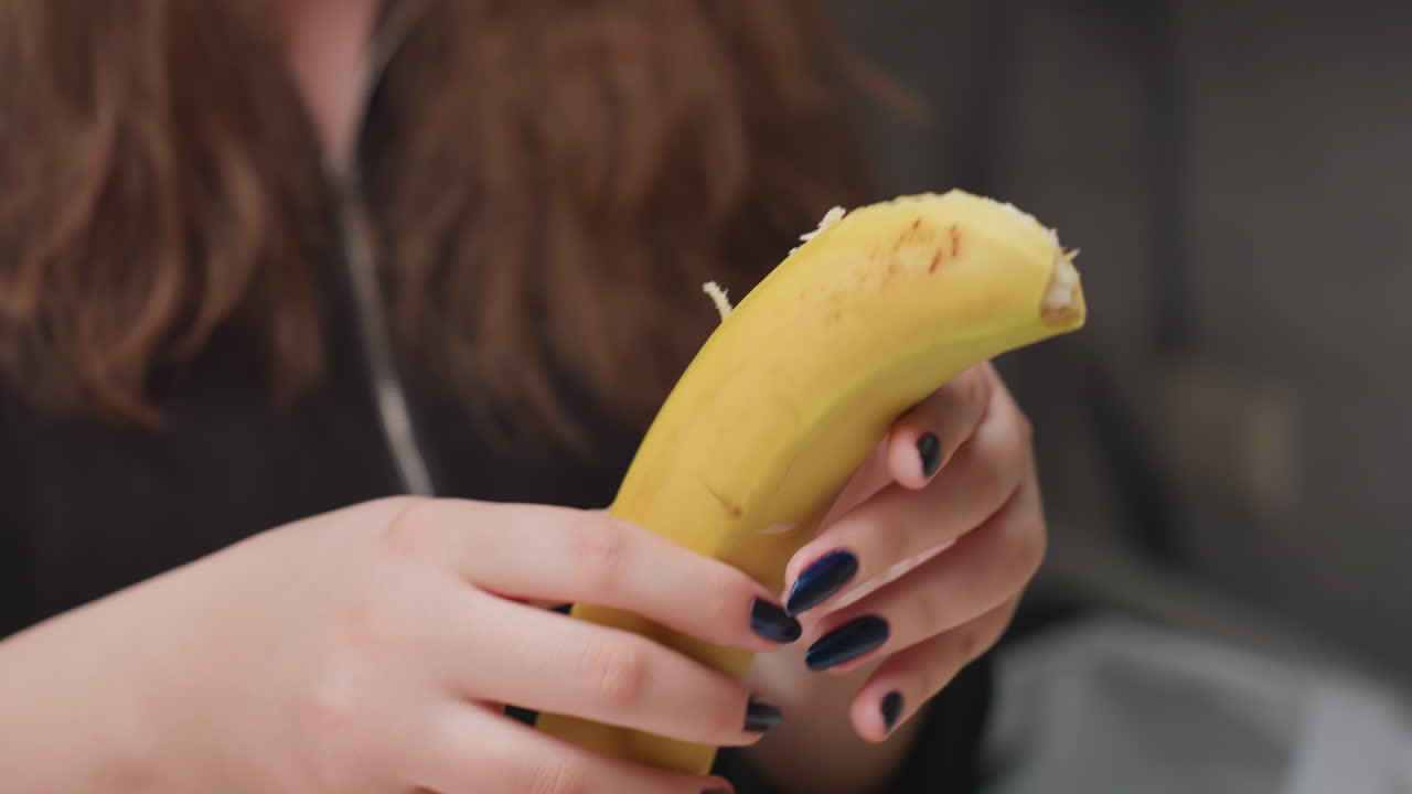 Close up hands peel banana beside apple and orange on white table, blue manicure visible, soft kitchen blur, fresh fruit prep moment, clean counter, gentle motion, natural light highlights textures