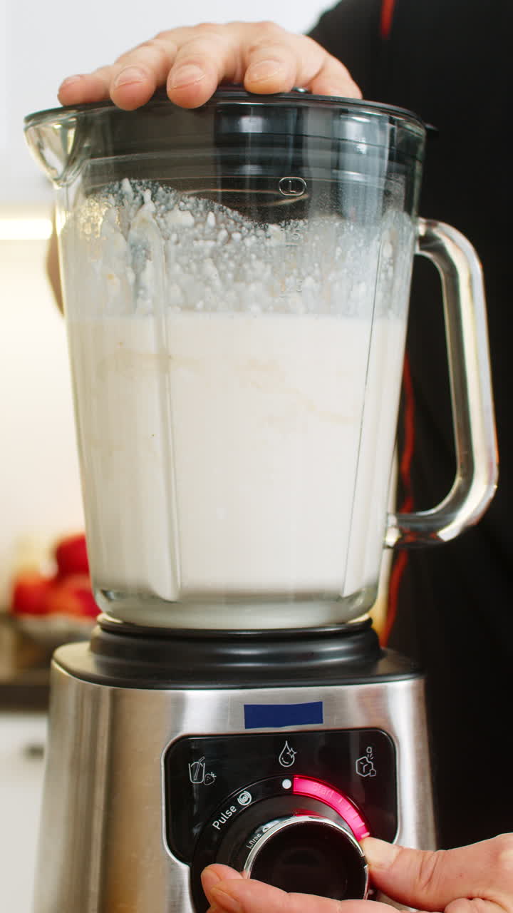 Uomo che usa un frullatore in una cucina di casa per preparare un frullato sano con banana, latte, ricotta e proteine del siero del latte