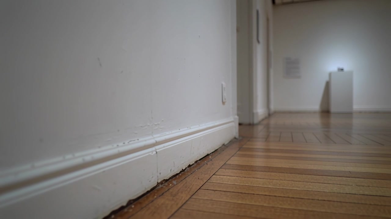 Tracking low camera moving down hallway, highlighting flaking baseboard and lit plinth, copy space