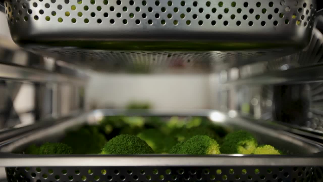 Fresh broccoli steaming in an industrial kitchen oven, from an interior perspective, shallow focus