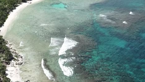 drone moving back and up over green ocean waves into rocky shoreline