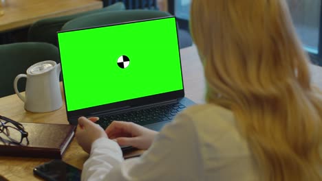 mockup view of woman using laptop with blank green screen in modern loft cafe.