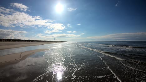 Aerial,-low,-drone-shot-over-calm-waves-on-a-beach,-on-Langeoog-island,-on-a-sunny-day,-in-North-Germany