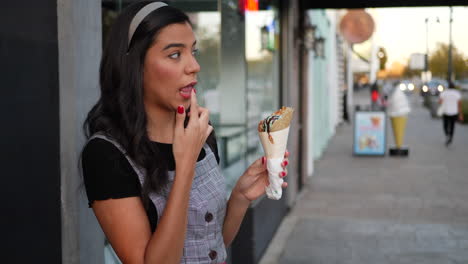 a cute young hispanic woman licking an ice cream cone and smiling with happiness at a dessert shop on a city street slow motion