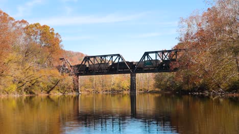 train crossing bridge over river during autumn from the viewpoint of a boat on the water in full hd