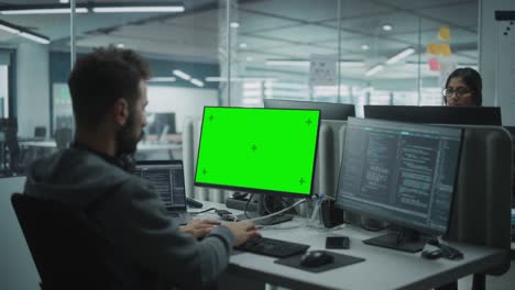 oficina multi-étnica: programador que trabaja en una computadora con pantalla verde con pantalla de tecla croma. ingeniero de software masculino desarrollando aplicación, programa, videojuego. terminal con lenguaje de código. disparo sobre el hombro